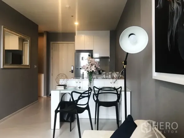 Condominium for sale in Khlong Toei, Bangkok - Open-plan dining area and compact kitchen with white cabinetry and black chairs.