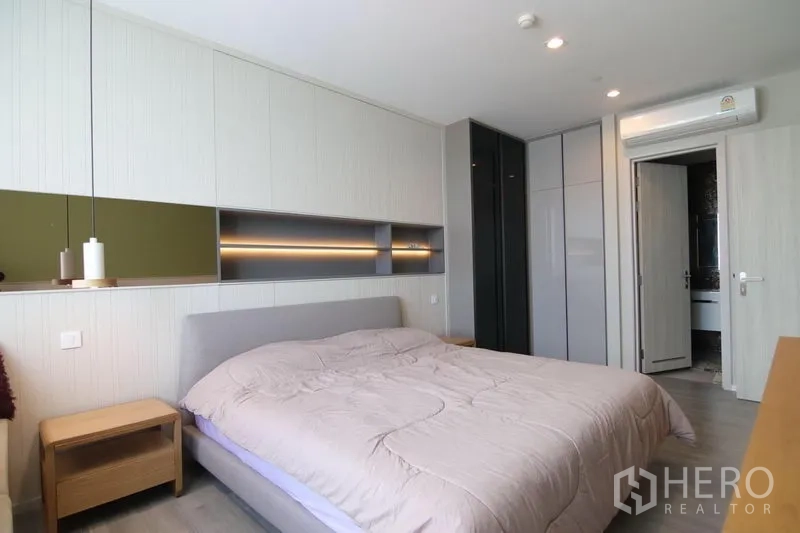 Condominium for rent in Bang Sue, Bangkok - Bright master bedroom with built-in headboard shelving, large wardrobes, and door to adjacent bathroom.