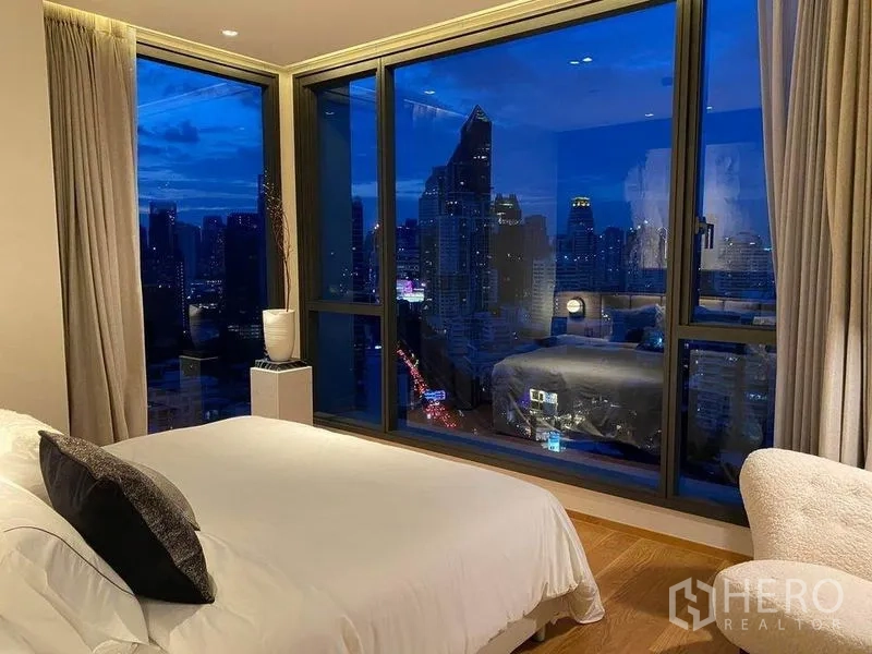 Condominium for rent or sale in Khlong Toei, Bangkok - Master bedroom with floor-to-ceiling corner windows showcasing Bangkok’s skyline at night.