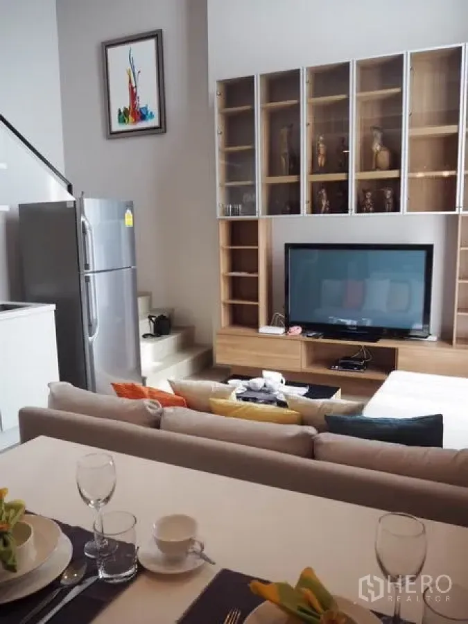 Condominium for rent in Ratchathewi, Bangkok - Open-plan living room with TV console, built-in shelving, sofa and stainless refrigerator in a modern Ratchathewi condo.