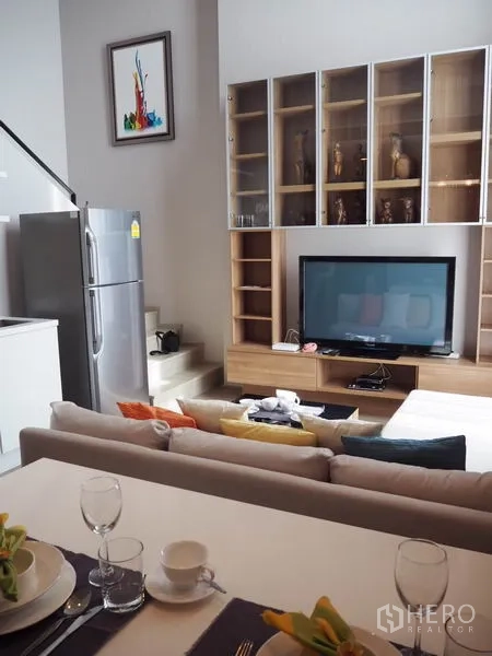 Condominium for rent in Ratchathewi, Bangkok - Open-plan living room with TV console, built-in shelving, sofa and stainless refrigerator in a modern Ratchathewi condo.