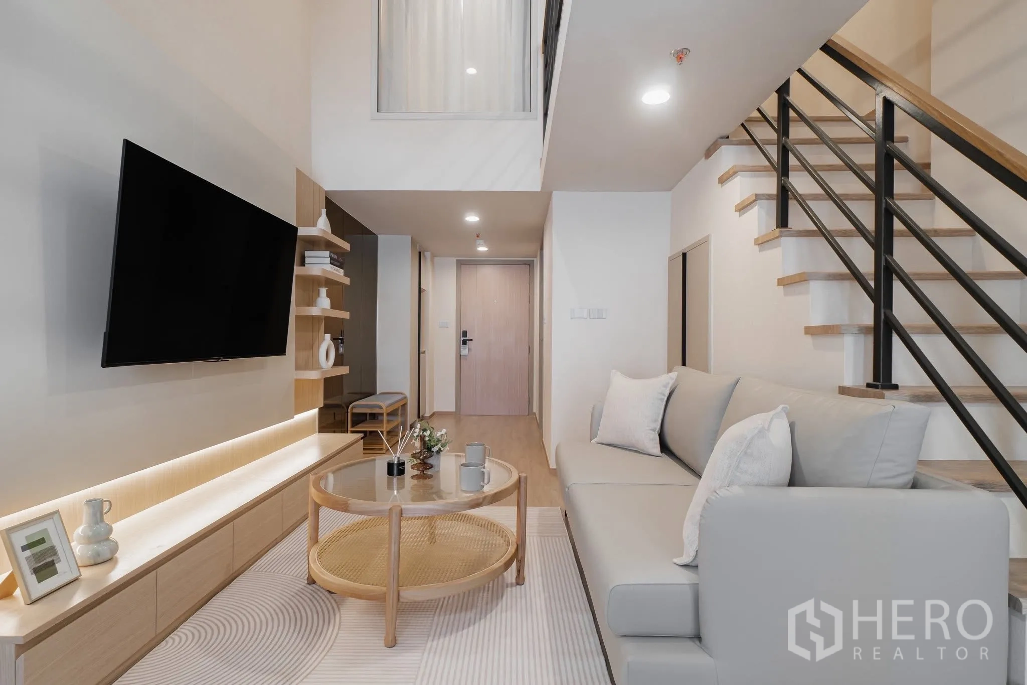 公寓 for rent in Bang Rak, Bangkok - 挑高客厅配沙发、壁挂电视、木质柜体、圆形玻璃茶几及通往夹层的楼梯，采光明亮。