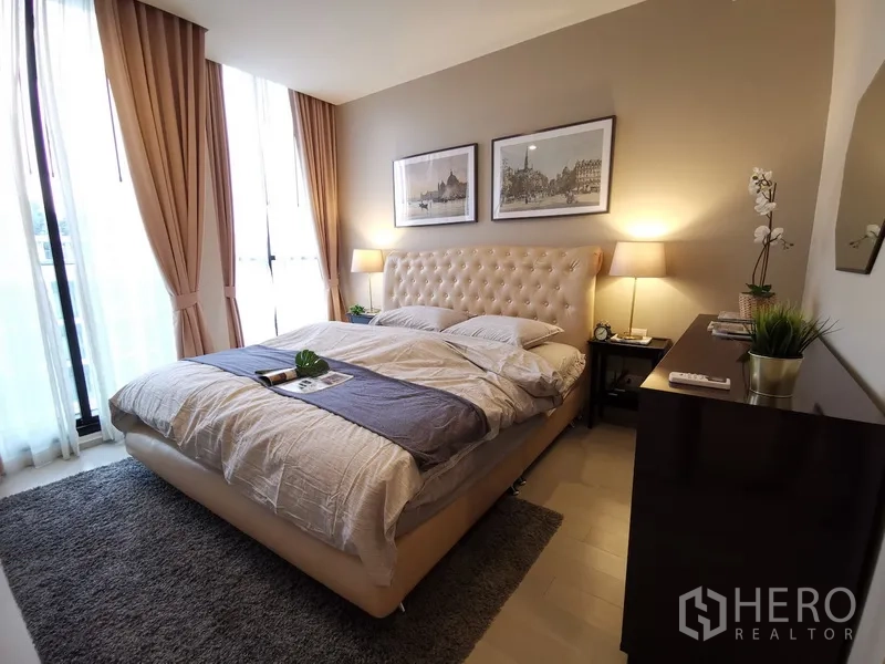 คอนโด ให้เช่าในPathum Wan, Bangkok - ห้องนอนสว่าง เตียงหัวเตียงบุหนัง โคมไฟข้างเตียง และหน้าต่างเต็มผนังพร้อมผ้าม่านสีเบจ