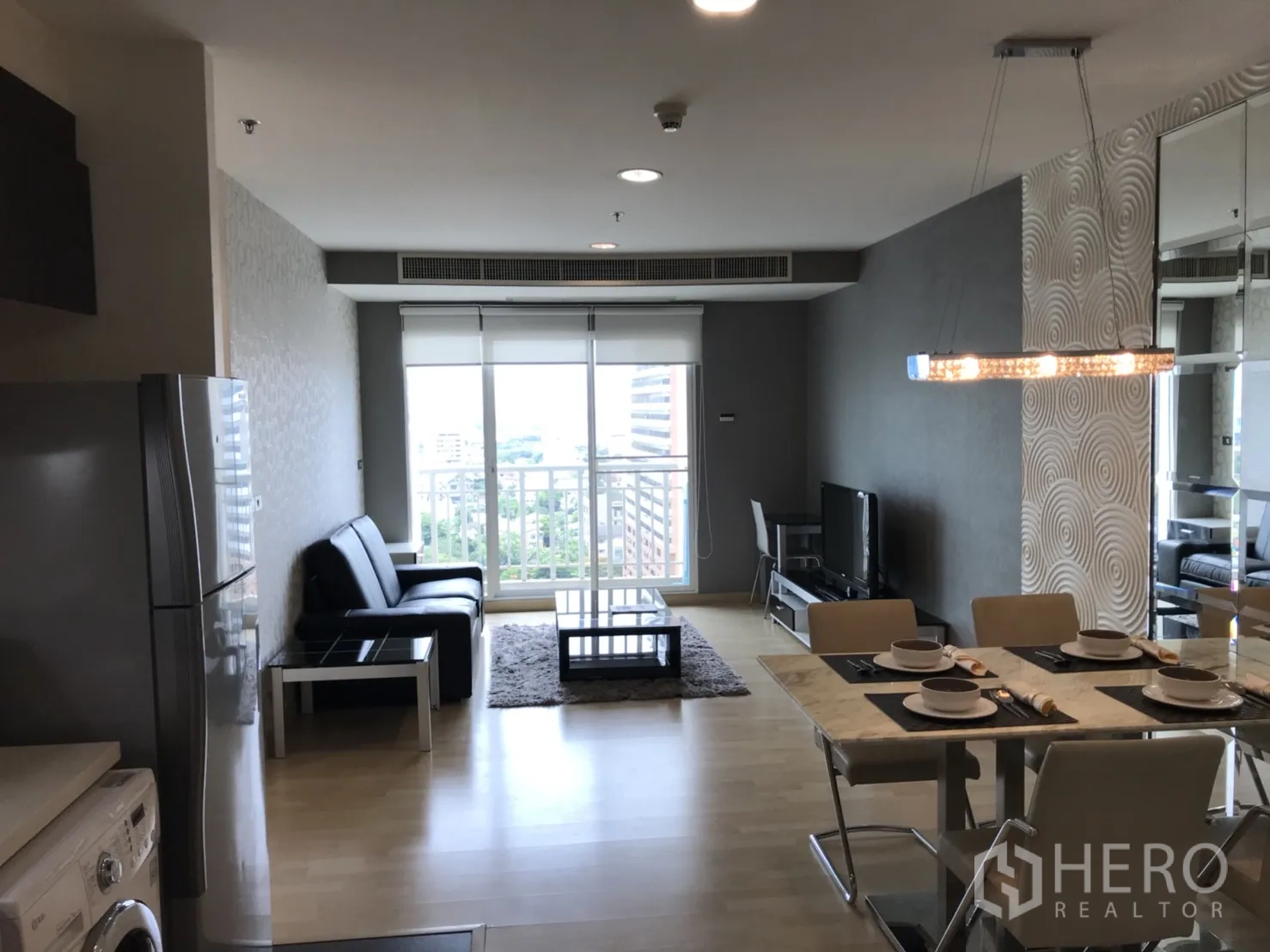 Condominium for rent in Watthana, Bangkok - Open-plan living and dining room with wood floors, pendant lighting, and a balcony offering city views.