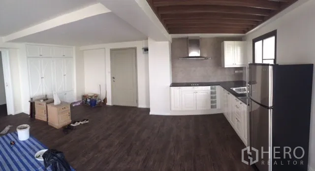 Condominium for rent or sale in Chatuchak, Bangkok - Open-plan room featuring a beamed ceiling, white kitchen, and built-in storage cabinets.