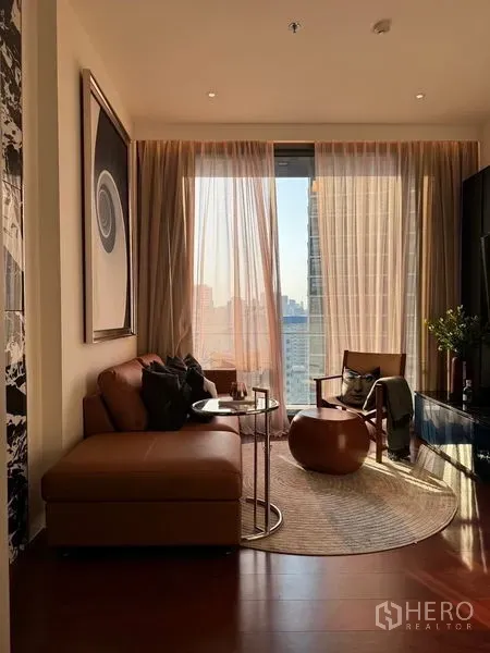 Condominium for sale in Watthana, Bangkok - Living room panorama with sofa, armchair and Bangkok skyline beyond a floor-to-ceiling window.