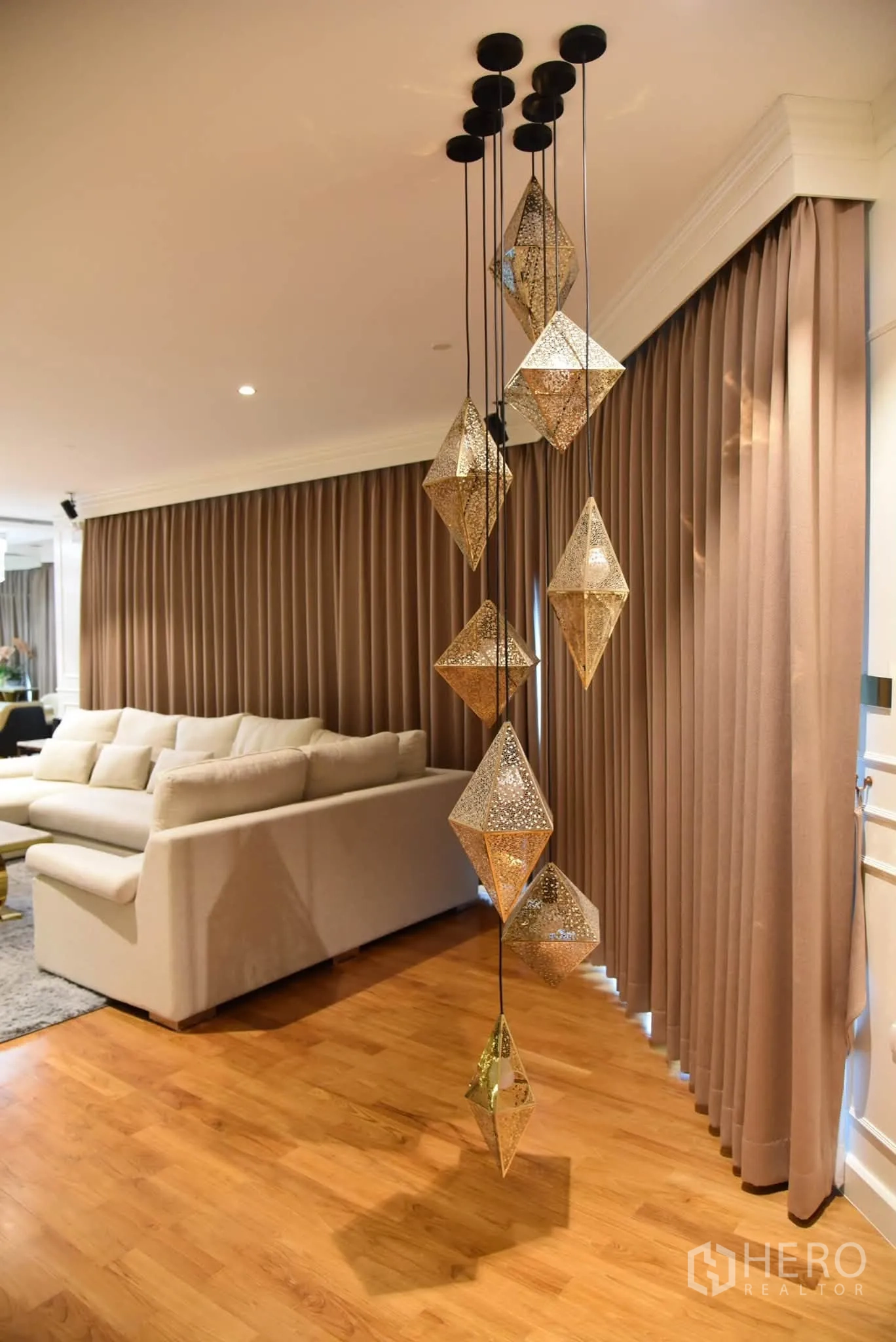 Condominium for sale in Khlong San, Bangkok - Statement pendant lights beside a beige sectional sofa and full-length curtains.