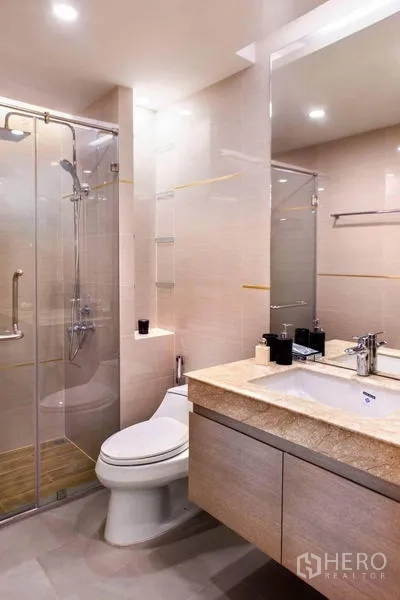 Condominium for rent in Huai Khwang, Bangkok - Modern bathroom with glass shower enclosure, toilet and stone-top vanity.
