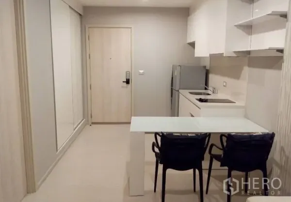 คอนโด ให้เช่าในKhlong Toei, Bangkok - มุมครัวขนาดกะทัดรัดตู้สีขาว มีตู้เย็น เตาไฟฟ้า และโต๊ะอาหารกระจกใกล้ประตูทางเข้า