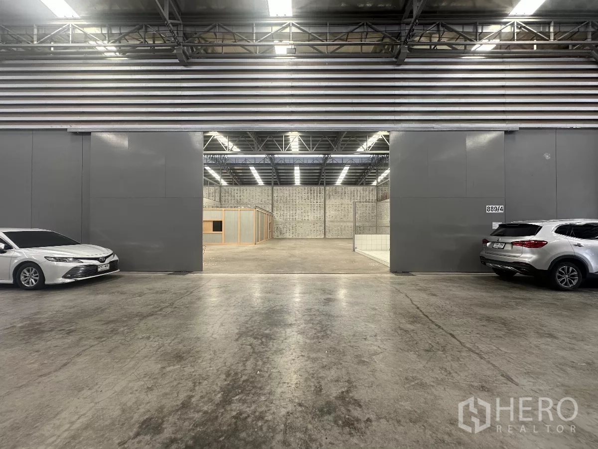 Warehouse for rent in Khlong Toei, Bangkok - Wide sliding warehouse entrance with high roof and concrete driveway, cars parked on both sides.