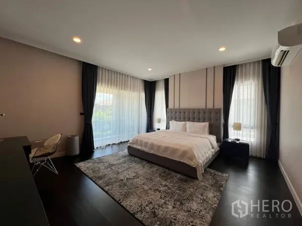 Detached House for rent in Bang Kapi, Bangkok - Spacious master bedroom with king bed, floor-to-ceiling windows, sheer curtains and dark wood flooring.