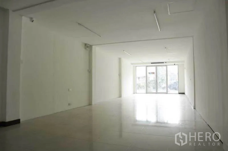 零售空间 出租在Watthana, Bangkok - 明亮的开放式零售空间，白色墙面、瓷砖地面，尽头为整面玻璃门面。