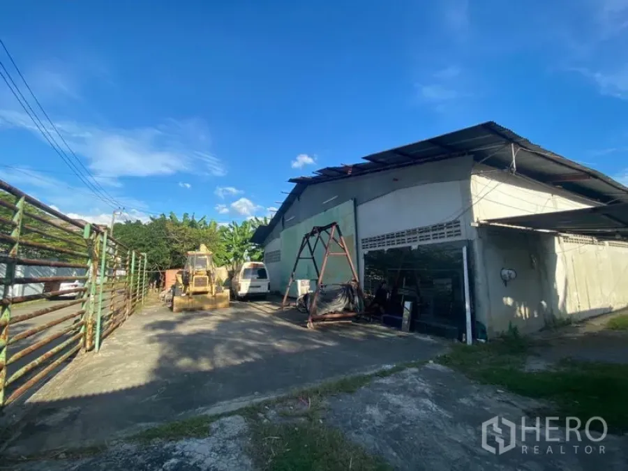 货栈 出租在Suan Luang, Bangkok - 素安隆仓库外观，宽阔混凝土地坪、金属屋顶，院内有机械与面包车，蓝天下采光良好。