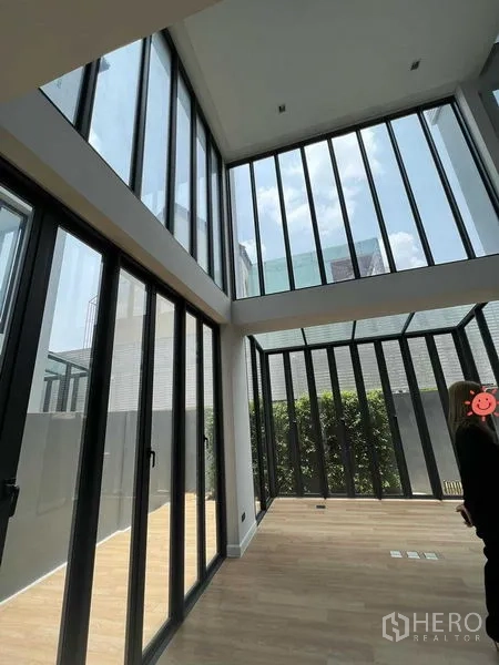 Home Office for sale in Wang Thonglang, Bangkok - Double-height living area with floor-to-ceiling glass walls, warm wood floors and greenery in a modern home office.