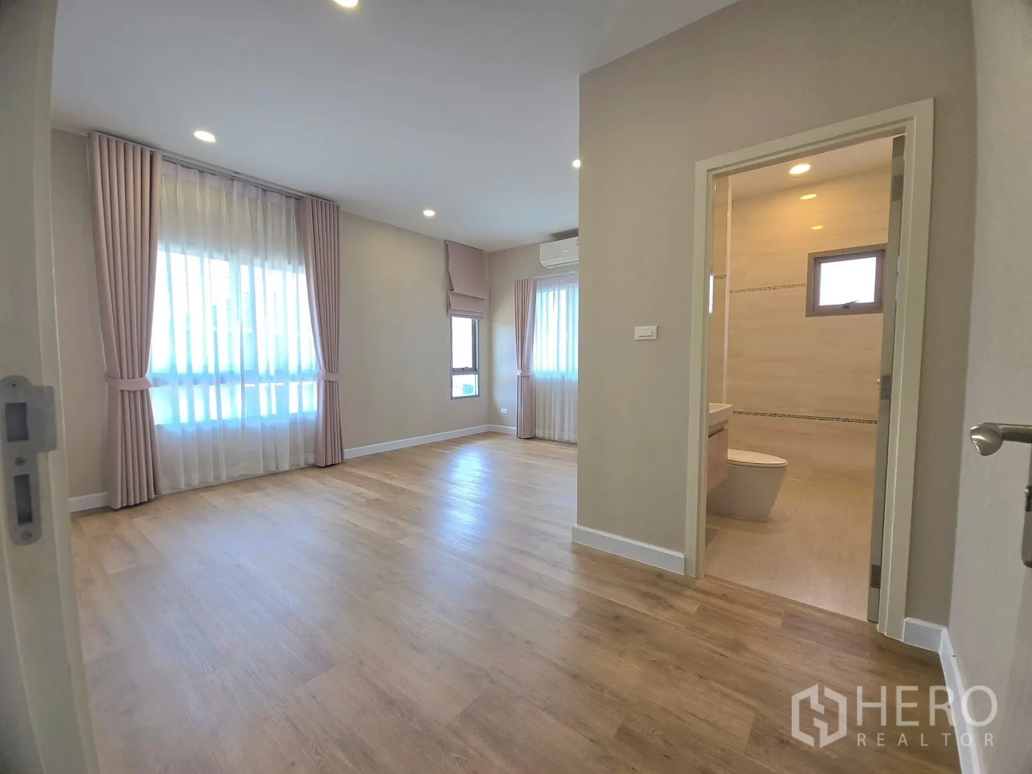 Detached House for rent in Lat Krabang, Bangkok - Spacious bedroom with wood flooring and an ensuite bathroom entrance.
