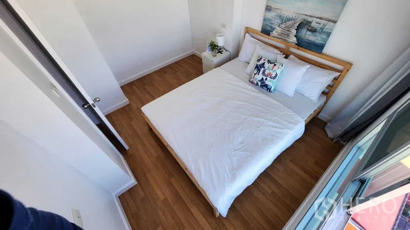 公寓 出售在Yan Nawa, Bangkok - 明亮卧室，木地板、白色床品、床头柜与通向阳台的窗。