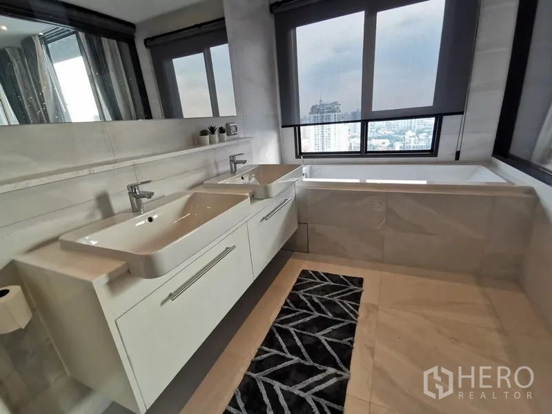 Condominium for rent or sale in Watthana, Bangkok - Bright en-suite bathroom featuring a double vanity and bathtub beside large windows with city skyline views.