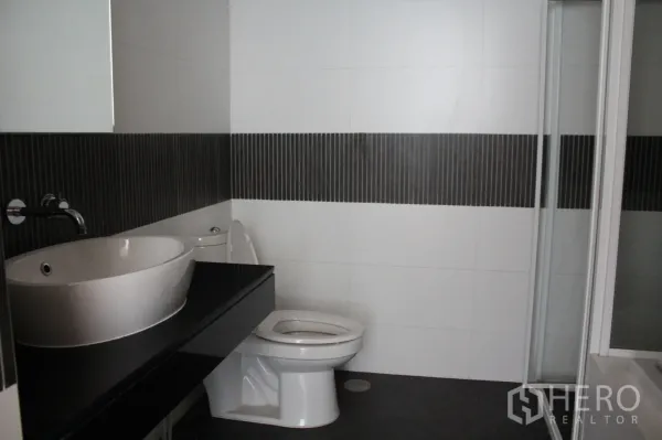 公寓 出租在Sathon, Bangkok - 现代浴室，台上盆与黑色台面、坐便器及玻璃淋浴间。