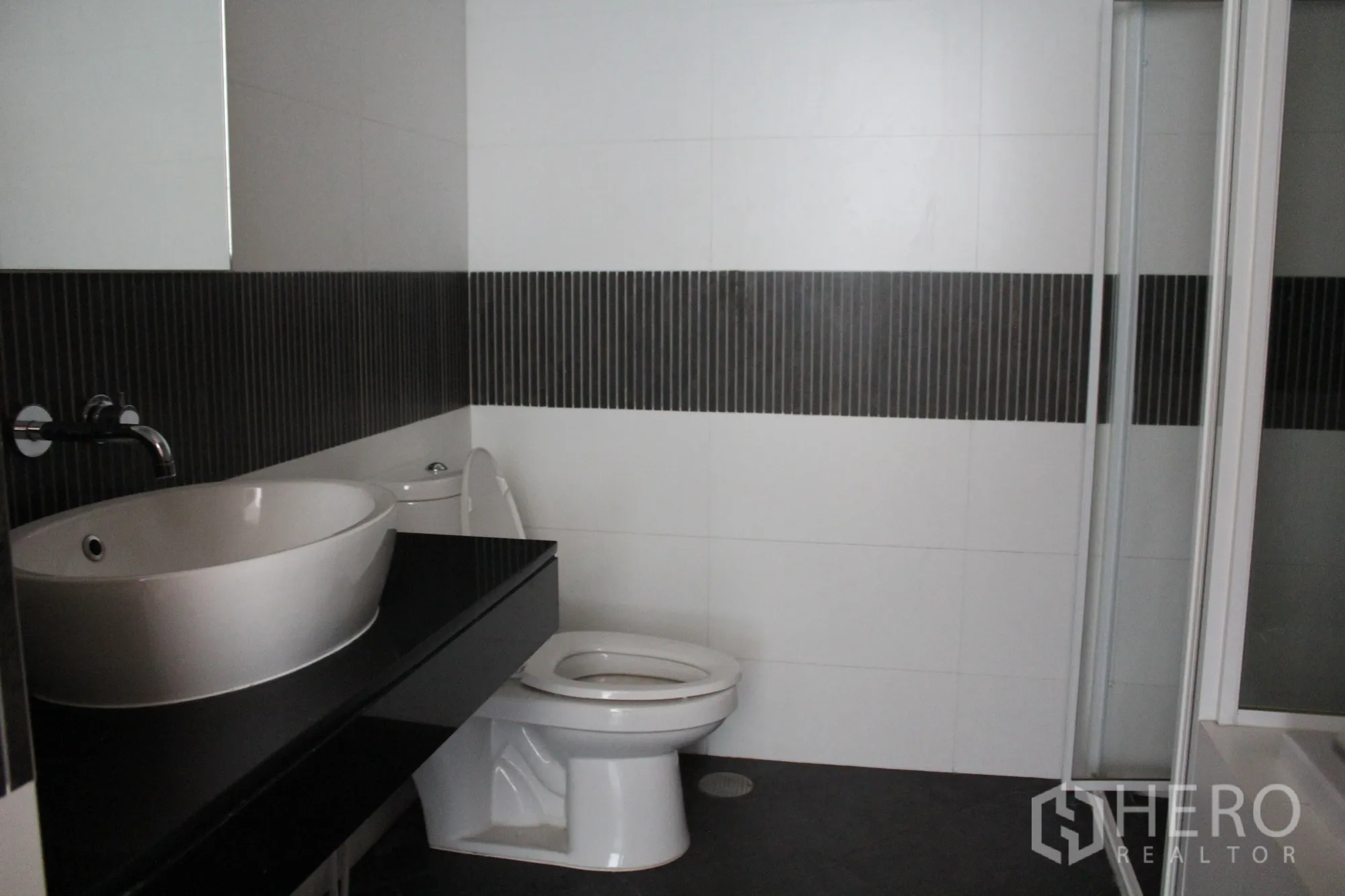 公寓 出租在Sathon, Bangkok - 现代浴室，台上盆与黑色台面、坐便器及玻璃淋浴间。