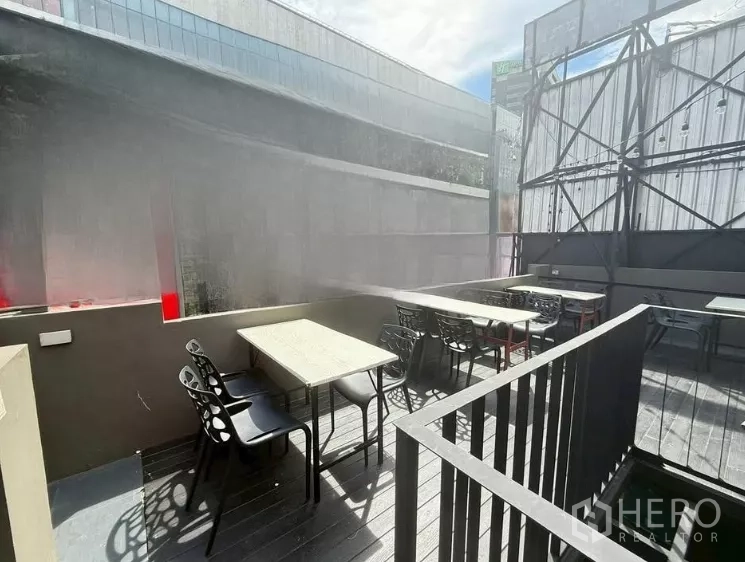 零售空间 出租在Watthana, Bangkok - 阳光充足的屋顶用餐区，数张桌子与黑色椅子靠近护栏