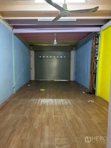 Shophouse for rent in Samphanthawong, Bangkok - Long ground-floor space with ceiling fan and a secure metal roll-up shutter, suitable for a storefront or loading area.
