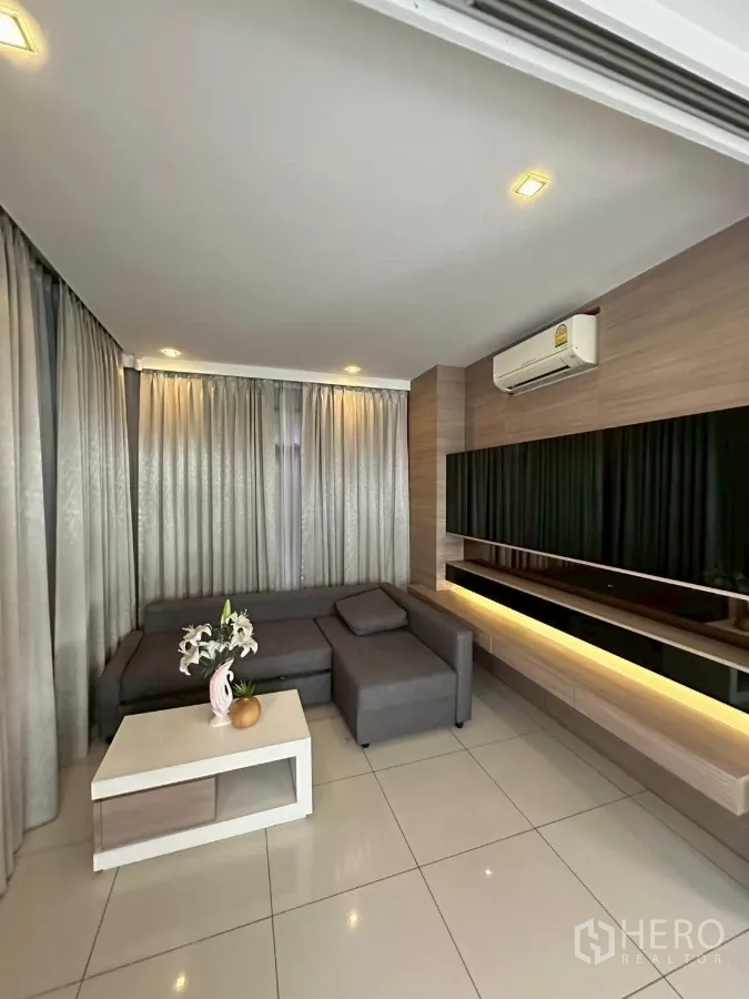 Detached House for sale in Bang Lamung, Chon Buri - Cozy lounge with gray L-shaped sofa, curtains and floating shelf.