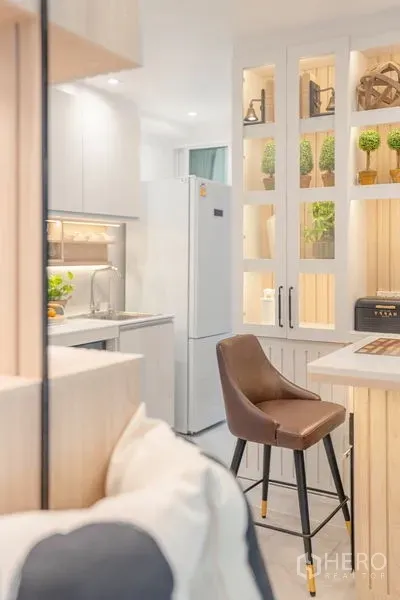 Condominium for sale in Yan Nawa, Bangkok - Compact kitchen view showing breakfast bar with leather stool, tall white refrigerator, and illuminated display shelving.