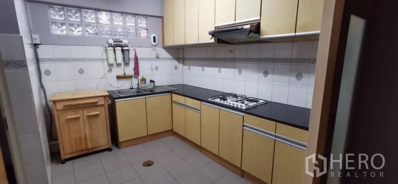Townhouse for rent in Watthana, Bangkok - Fitted L-shaped kitchen with gas hob, hood, ample cabinets and tiled backsplash
