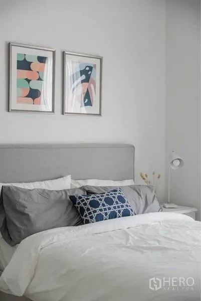 Condominium for sale in Huai Khwang, Bangkok - Minimal bedroom featuring an upholstered headboard, framed abstract art, and a bedside lamp.