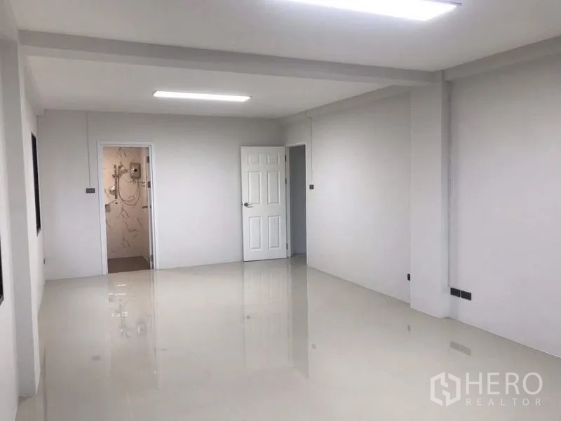Warehouse for rent or sale in Nong Chok, Bangkok - Open-plan office area with LED lighting, white doors and polished floor next to a tiled bathroom.