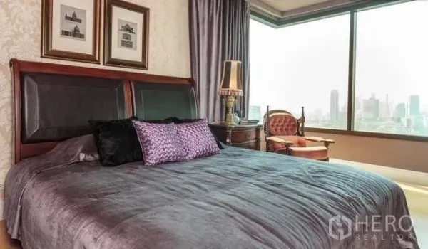 Condominium for rent or sale in Khlong Toei, Bangkok - Master bedroom with large window and skyline view, classic wooden furniture.