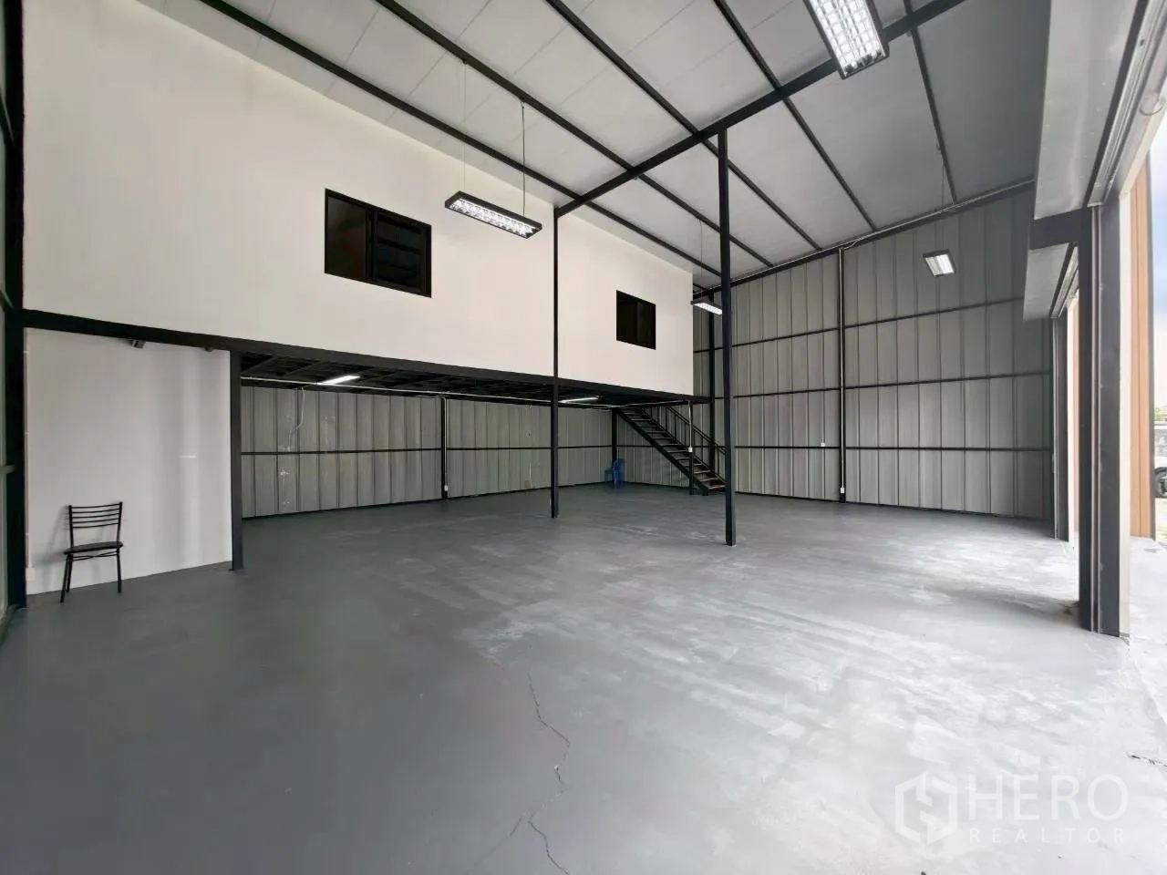 Warehouse for rent in Suan Luang, Bangkok - Open warehouse space with mezzanine, pendant lights, and large roller doors providing easy loading access.