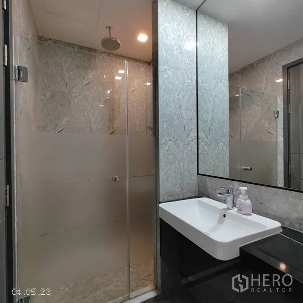 Condominium for rent in Watthana, Bangkok - Glass-enclosed shower with rain head beside a sleek vanity in the tiled bathroom.