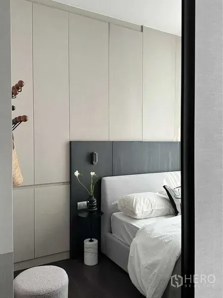 Condominium for rent or sale in Watthana, Bangkok - Cozy bedroom corner with built-in wardrobes, dark headboard, small stool and vase.
