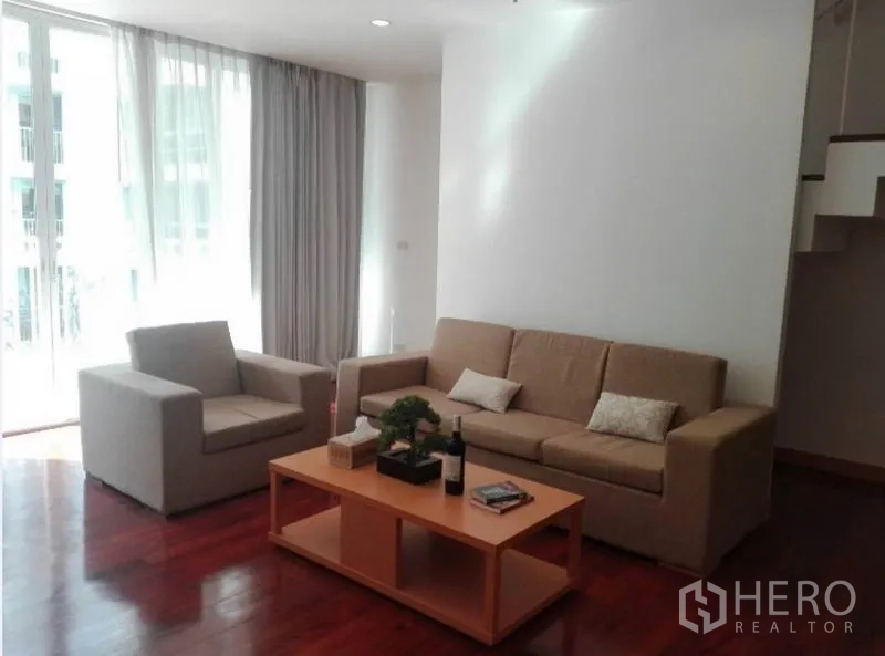 Condominium for rent in Watthana, Bangkok - Bright living room with sofa set, armchair, coffee table, and floor-to-ceiling windows.