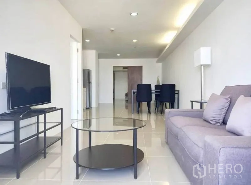 公寓 出租在Khlong Toei, Bangkok - 明亮的客厅，灰色沙发、玻璃茶几、电视柜与用餐区一体。