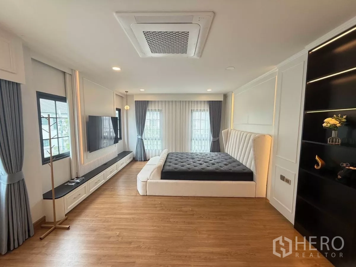 Detached House for rent in Bang Phli, Samut Prakan - Master bedroom with upholstered bed, wood floors, large windows and a TV wall unit.
