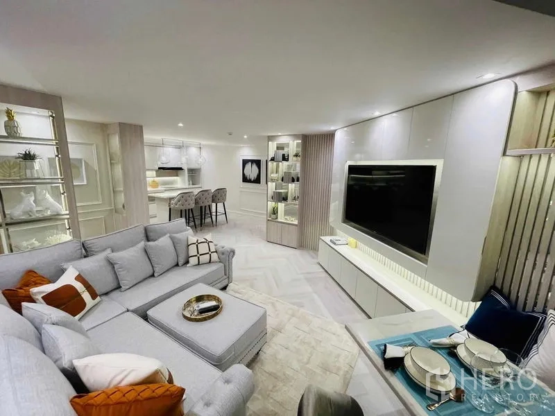 Condominium for sale in Yan Nawa, Bangkok - Wide shot of elegant living room with sectional sofa, rug, and shelving.