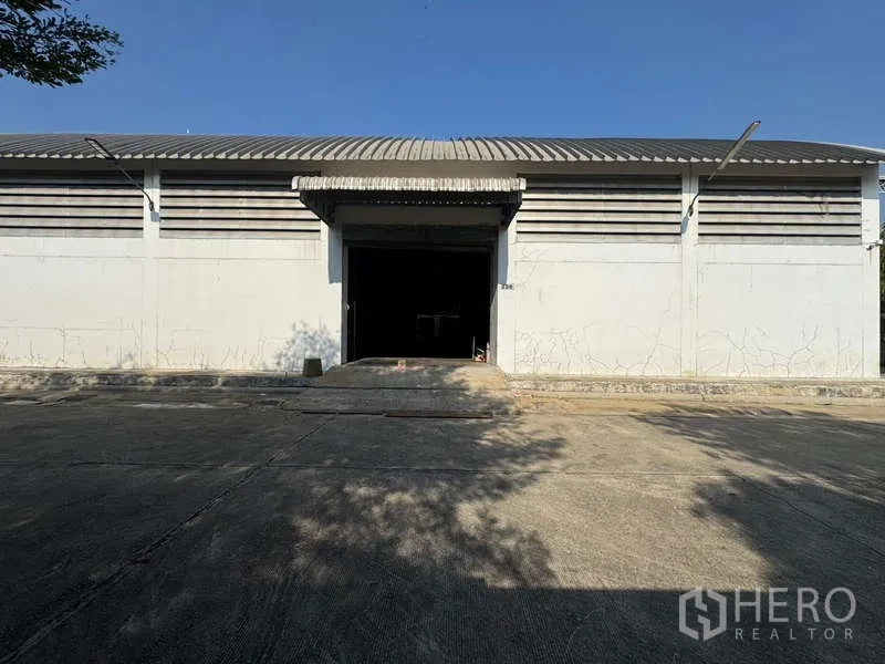 Warehouse for rent in Photharam, Ratchaburi - Front loading dock with ramp, roller shutter door, and ample driveway.