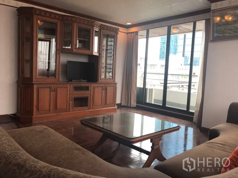 คอนโด ให้เช่าในKhlong Toei, Bangkok - ห้องนั่งเล่นสว่าง ตู้ทีวีบิลท์อินไม้ และประตูกระจกสไลด์ออกระเบียงวิวเมือง