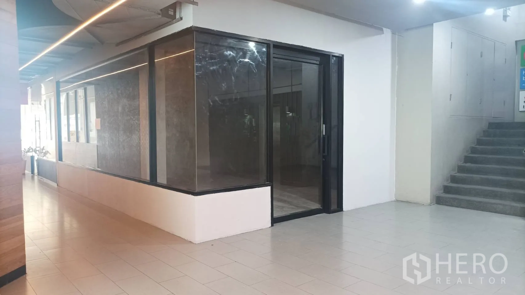 零售空间 出租 - 一层转角商铺，黑色框架玻璃立面，瓷砖走廊与楼梯。