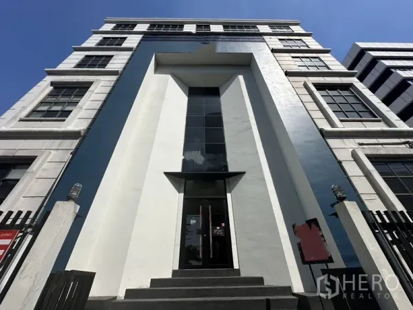 零售空间 出租在Phra Khanong, Bangkok - 帕卡农区现代商业建筑外观，高挑玻璃入口与几何立面，蓝天下的近景。