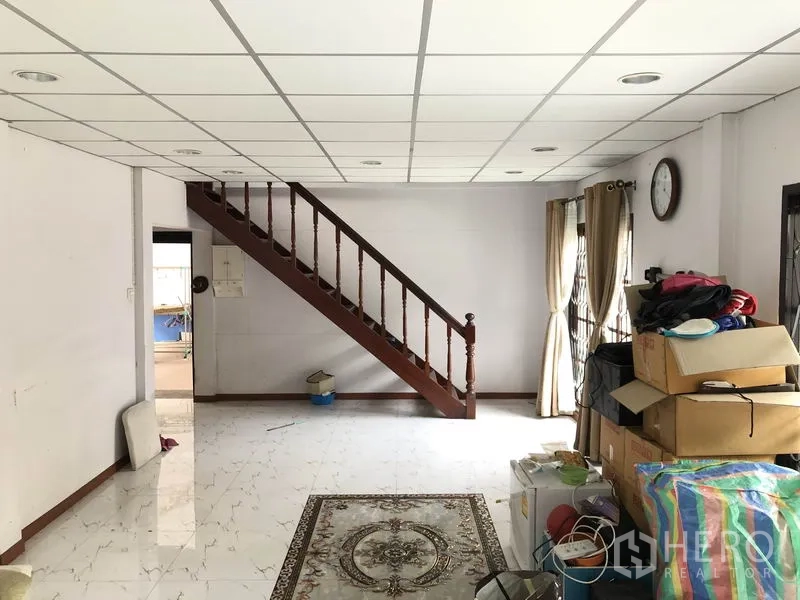 独立式住宅 出售在Pak Kret, Nonthaburi - 开放式起居区，木楼梯通往二层，窗帘与亮面地砖。