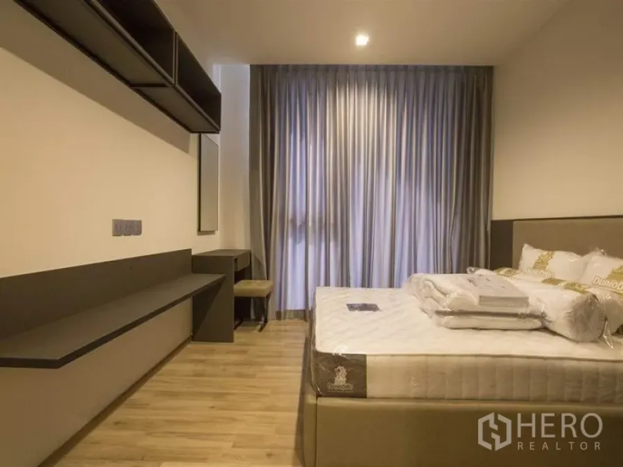 Condominium for rent in Chatuchak, Bangkok - Bedroom with queen bed, floor-to-ceiling curtains, built-in desk and shelving on wood floors.