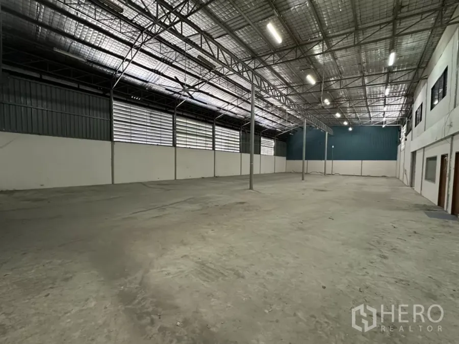 Warehouse for rent in Suan Luang, Bangkok - Spacious warehouse interior in Suan Luang with high steel truss roof, insulated ceiling, concrete floor, louvered side vents, and attached office block.