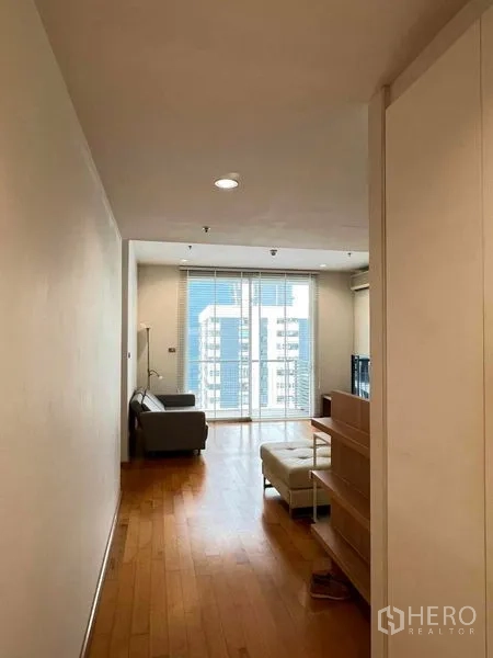 公寓 出租在Ratchathewi, Bangkok - 明亮走廊通向客厅，木地板、沙发与可看城市景观的阳台。