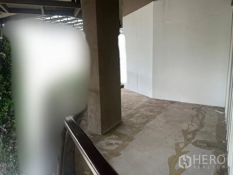 零售空间 出租在Watthana, Bangkok - 开放走道与未装修的店面外侧，混凝土立柱、白色临时围挡和水泥地面。