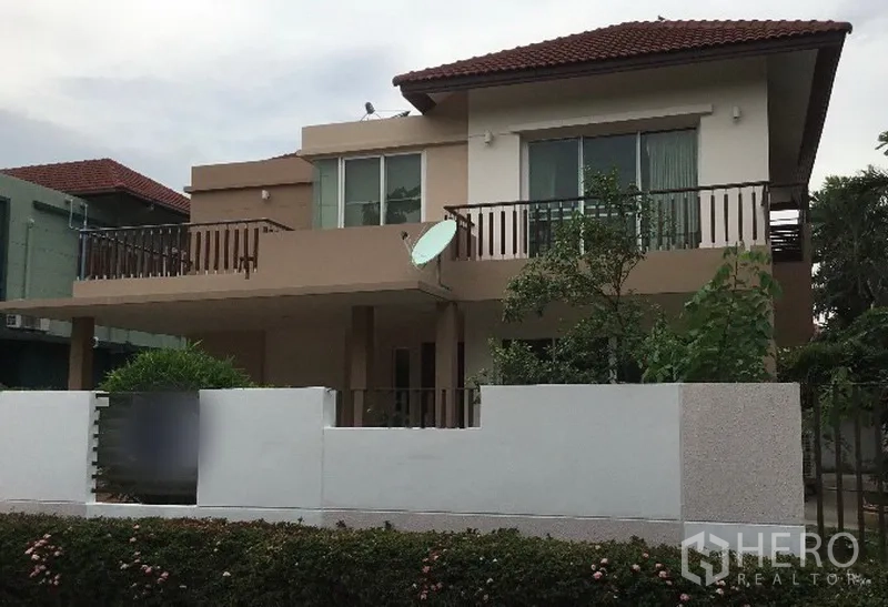 Detached House for rent in Bang Phli, Samut Prakan - Two-storey detached house with tiled roof, balconies and walled front garden in a quiet residential estate.