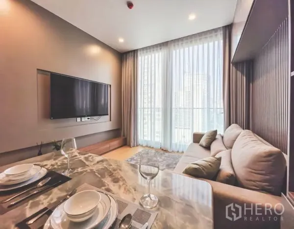 Condominium for rent in Bang Rak, Bangkok - Cozy lounge with sofa, TV wall, full-height curtains and a marble-top dining table.