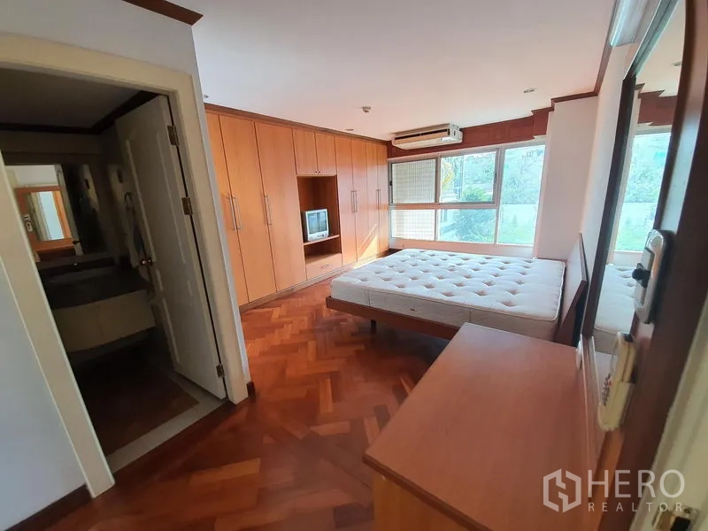 Condominium for rent in Pathum Wan, Bangkok - Primary bedroom with parquet flooring, built-in wardrobes, large windows, and ensuite access.